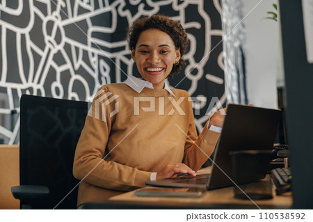 Smiling business woman using laptop while sitting on modern office background  110538592