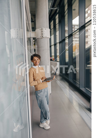 Smiling female manager using laptop while standing on office background and looks camera 110538615