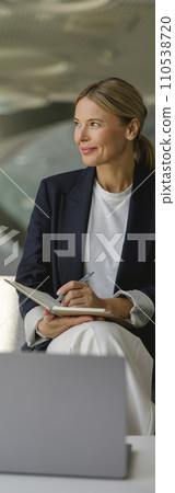 Confident female manager making notes in note pad sitting on modern office background 110538720