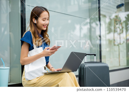 A beautiful woman works remotely on her laptop computer while waiting for her train. She's able to balance work and travel with ease, thanks to modern technology. new age of productivity. 110539470