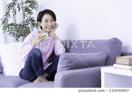 Middle-aged woman relaxing on the sofa while drinking coffee 110540067