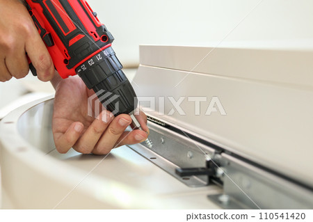 man assembling white table furniture at home using cordless screwdriver 110541420