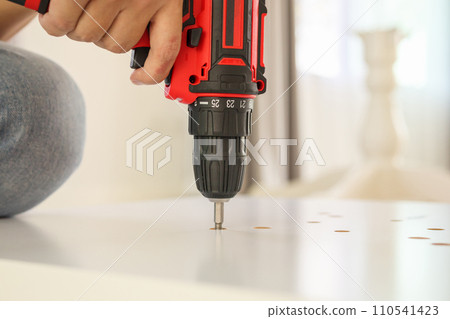 man assembling white table furniture at home using cordless screwdriver 110541423
