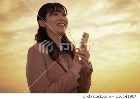 夕陽下使用智慧型手機的女人 110541904