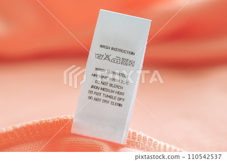 White laundry care washing instructions clothes label on pink cotton shirt White laundry care washing instructions clothes label on pink cotton shirt 110542537