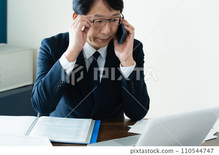 商人一邊看電腦一邊用智慧型手機交談 110544747