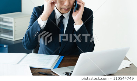 商人一邊看電腦一邊用智慧型手機交談 110544749