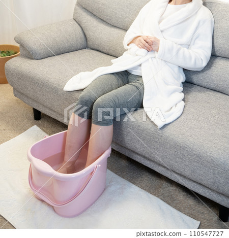 坐在沙發上使用足浴的女人的腳 坐在沙發上使用足浴的女人的腳 110547727