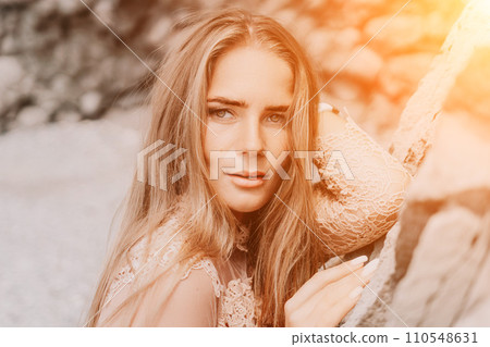 Woman summer travel sea. Happy tourist in beige dress enjoy taking picture outdoors for memories. Woman traveler posing on the beach surrounded by volcanic mountains, sharing travel adventure journey 110548631