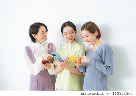 A group of middle-aged women talking while looking at their smartphones A group of middle-aged women talking while looking at their smartphones 110551565