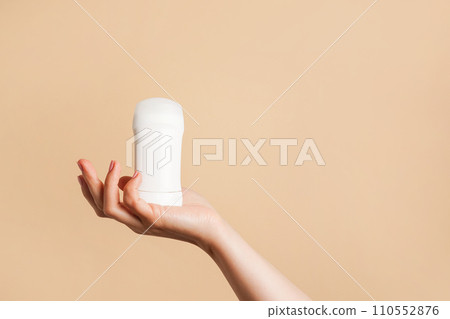 Female hand holds white body deodorant on beige background, copy space 110552876