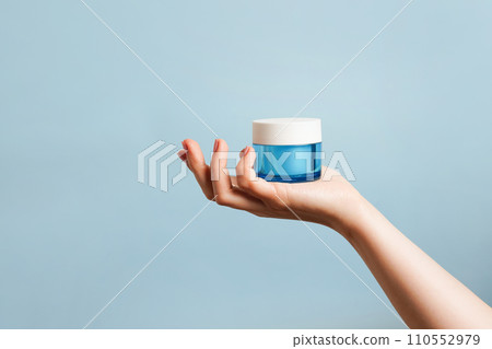Woman holding a blue glass jar of skin cream on blue background. Skin care concept. Moisturizing cream in female hand . Beauty treatment. Copy space 110552979