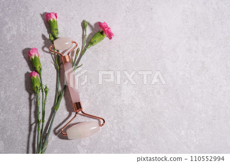 Facial jade massage gua sha roller with trendy shadows and flowers on concrete background, beauty anti aging tools Facial jade massage gua sha roller with trendy shadows and flowers on concrete background, beauty anti aging tools 110552994