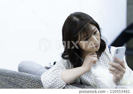 Middle-aged woman using a smartphone on the sofa in the living room Middle-aged woman using a smartphone on the sofa in the living room 110553481