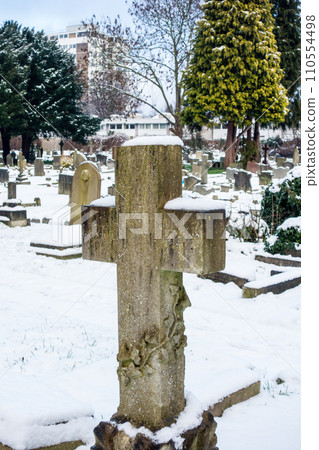 A snowy cemetery with a stone cross, a cityscape on the outskirts of London A snowy cemetery with a stone cross, a cityscape on the outskirts of London 110554498