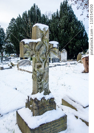 A snowy cemetery with a stone cross, a cityscape on the outskirts of London A snowy cemetery with a stone cross, a cityscape on the outskirts of London 110554500