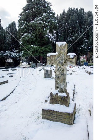 A snowy cemetery with a stone cross, a cityscape on the outskirts of London 110554504
