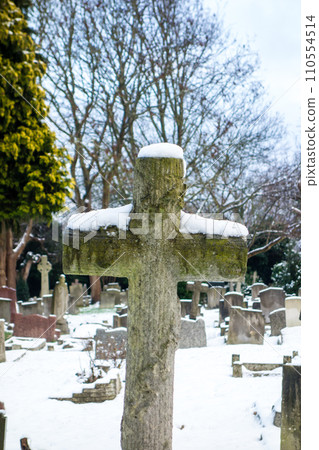 A snowy cemetery with a stone cross, a cityscape on the outskirts of London A snowy cemetery with a stone cross, a cityscape on the outskirts of London 110554514