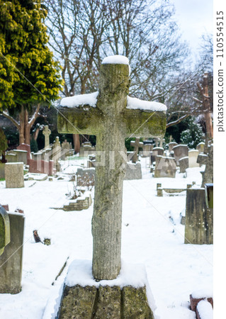 A snowy cemetery with a stone cross, a cityscape on the outskirts of London A snowy cemetery with a stone cross, a cityscape on the outskirts of London 110554515