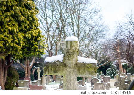 A snowy cemetery with a stone cross, a cityscape on the outskirts of London A snowy cemetery with a stone cross, a cityscape on the outskirts of London 110554516