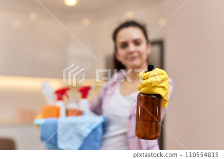 Woman in rubber protective yellow gloves spraying detergent and holding bucket with cleaning tools. house chores. copy space Woman in rubber protective yellow gloves spraying detergent and holding bucket with cleaning tools. house chores. copy space 110554815