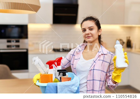 Woman in rubber protective yellow gloves holding bucket with cleaning detergents and rags . house chores. Woman in rubber protective yellow gloves holding bucket with cleaning detergents and rags . house chores. 110554816