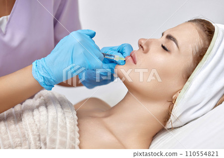 cosmetologist makes injections to enlarge the lips of beautiful woman. Woman in beauty salon. plastic surgery. cosmetologist makes injections to enlarge the lips of beautiful woman. Woman in beauty salon. plastic surgery. 110554821