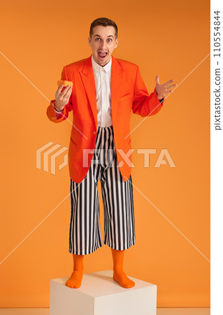 extravagant funny young man in orange jacket and striped pants on yellow background. extravagant funny young man in orange jacket and striped pants on yellow background. 110554844