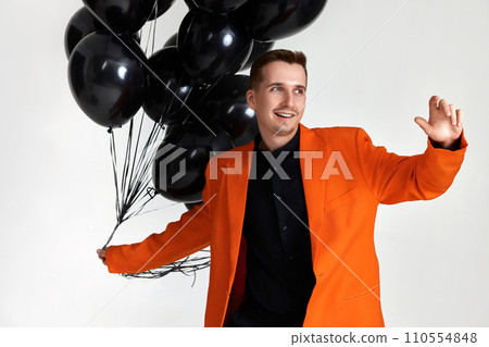 smiling guy in orange jacket with black air balloons on white background. birthday party smiling guy in orange jacket with black air balloons on white background. birthday party 110554848