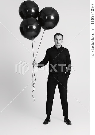 elegant caucasian man with bunch of black air balloons on white background. black and white elegant caucasian man with bunch of black air balloons on white background. black and white 110554850