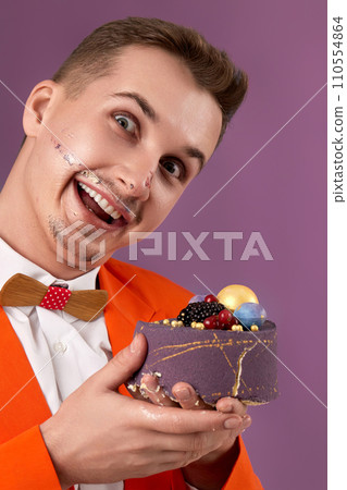 funny birthday man in orange jacket eating cake on purple background 110554864