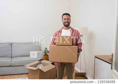 Happy man holds packed shipping boxes standing in newly renovated living room parcels with items for transportation by service and moving to new apartment Happy man holds packed shipping boxes standing in newly renovated living room parcels with items for transportation by service and moving to new apartment 110556089