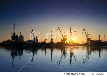 Sunset silhouettes cargo ships, cranes at sea port. Industrial loads freight at dock. Trade, transport infrastructure. Maritime logistics, global shipping. Clear sky reflects calm water. Sunset silhouettes cargo ships, cranes at sea port. Industrial loads freight at dock. Trade, transport infrastructure. Maritime logistics, global shipping. Clear sky reflects calm water. 110556502