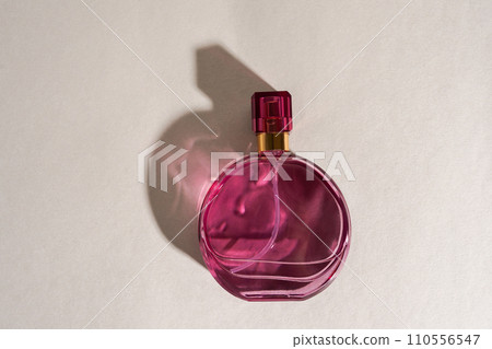 Pink perfume bottle with reflections and contrasting shadows on light gray background Pink perfume bottle with reflections and contrasting shadows on light gray background 110556547