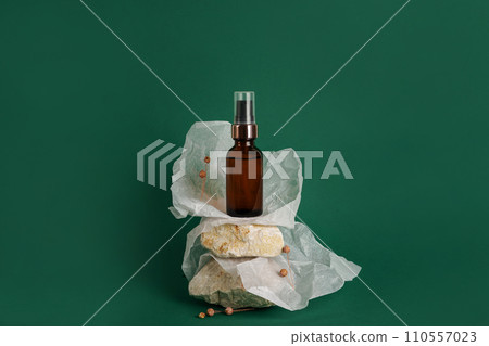 Glass bottle of moisturizing face serum, cosmetic oil on stones on green background. Eco natural cosmetics 110557023