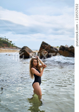 Attractive woman in swimsuit enjoys sea bath by rocky coast. Wellness lifestyle, tranquil nature escape. Female relaxes in water, summer travel vacation. Health, leisure, swimming, ocean view. Attractive woman in swimsuit enjoys sea bath by rocky coast. Wellness lifestyle, tranquil nature escape. Female relaxes in water, summer travel vacation. Health, leisure, swimming, ocean view. 110557032