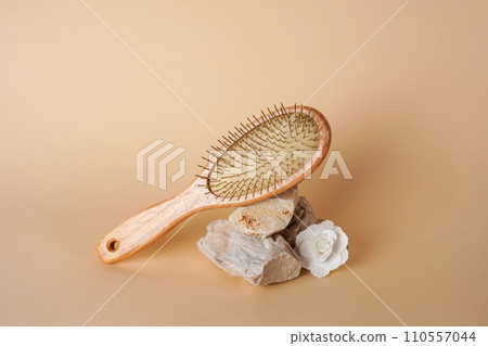 Close-up of a wooden hair brush on stone podium with flower on beige background 110557044