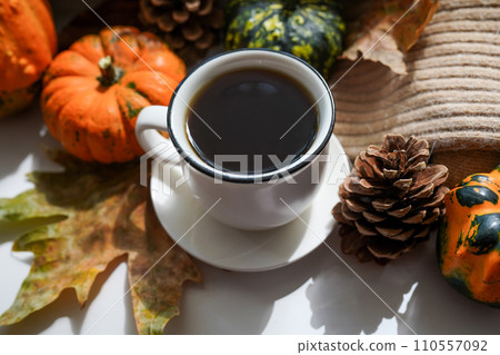 Autumn, fall leaves, hot steaming cup of coffee and a warm scarf on white table background. Seasonal, morning coffee, Sunday relaxing and still life concept 110557092