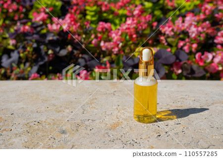 Glass bottle with dropper pipette with serum or essential oil on concrete background near pink flowers. Skin care cosmetic. Beauty concept for face body care Glass bottle with dropper pipette with serum or essential oil on concrete background near pink flowers. Skin care cosmetic. Beauty concept for face body care 110557285