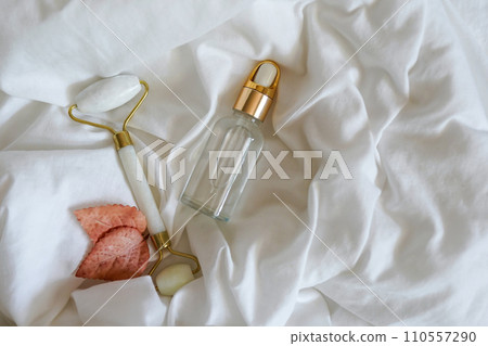 Glass bottle with oil, Gua sha stone for face massage and autumn leaves on white bed background. Cosmetic facial skin care and spa. Natural treatment concept 110557290