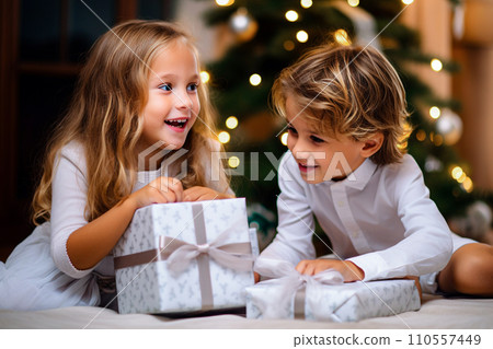 Cute little boy and girl opening Christmas gifts at home on Christmas Eve. Selective focu Cute little boy and girl opening Christmas gifts at home on Christmas Eve. Selective focu 110557449