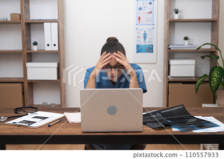 Pensive female doctor works at laptop resting head on hands tiredly exhausted young practitioner solves complex problems regarding patient treatment sitting in office 110557933