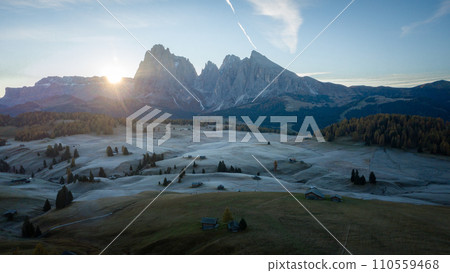Sun rising above high alpine pasture with huts from behind a wall of mountains, aerial, Dolomites Sun rising above high alpine pasture with huts from behind a wall of mountains, aerial, Dolomites 110559468