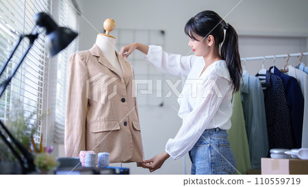 Young asian merchant women using measure tape to checking length size details of fashion clothes in mannequin while taking notes in clipboard and working about online shopping business in home office Young asian merchant women using measure tape to checking length size details of fashion clothes in mannequin while taking notes in clipboard and working about online shopping business in home office 110559719