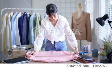 Young asian merchant women using measure tape to checking chest size details of fashion clothes on the table while taking notes in tablet and working about online shopping business in home office Young asian merchant women using measure tape to checking chest size details of fashion clothes on the table while taking notes in tablet and working about online shopping business in home office 110559720