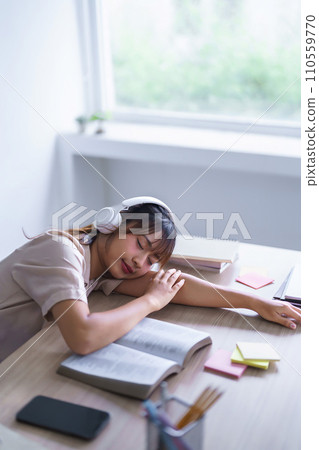 Young asian student in casual clothes wear headphones to listening music and sleep to resting on desk after reading a book and studying education knowledge to doing homework assignments in university 110559770