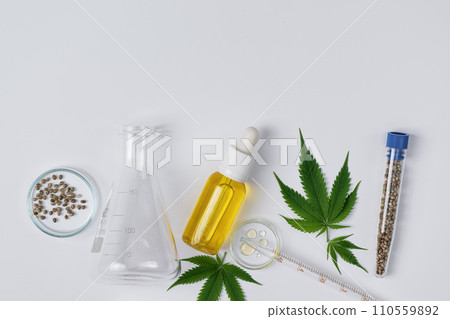Cannabis CBD oil and hemp leaves with laboratory glass top view. Laboratory glassware and cannabis sativa herb and hemp seeds. Cannabis herbal alternative medicine. 110559892