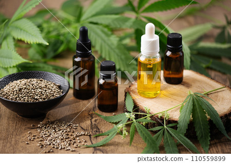 CBD hemp oil in a bottles and hemp seeds with cannabis leaf on wooden background. Hemp herbal alternative medicine. 110559899