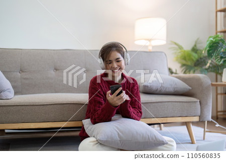 Young Asian woman in headphone listening to music while relax on sofa in living room at home Young Asian woman in headphone listening to music while relax on sofa in living room at home 110560835