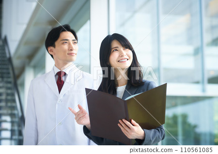 一位穿白大褂的男醫生和一位穿西裝的 MR 女商人在醫院走廊開會 一位穿白大褂的男醫生和一位穿西裝的 MR 女商人在醫院走廊開會 110561085